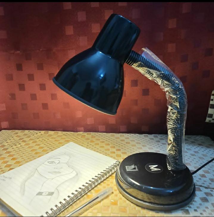 Black desk lamp with flexible neck on a table with a red checkered wall in the background